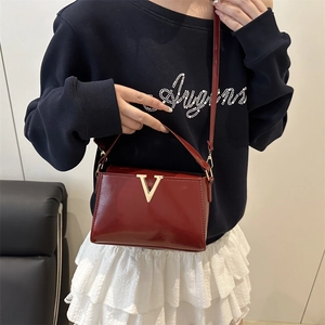Fashionable wine red patent leather handbag with gold V buckle shown on a model