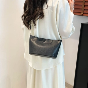 Sac seau bandoulière minimaliste en cuir noir à motif litchi porté par un mannequin
