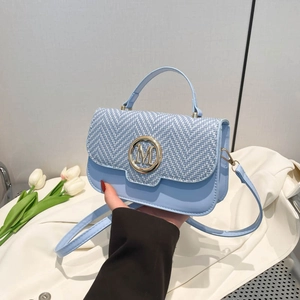 Light blue woven leather crossbody bag with golden M buckle held in a lifestyle setting