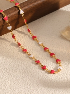 Detail of gold heart link necklace with pink, red, and white enamel on a wooden surface
