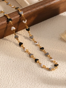 Detailed view of gold chain necklace with black, white, and grey enamel heart charms