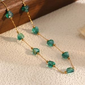 Golden chain necklace with heart-shaped green crystal beads on a wooden base