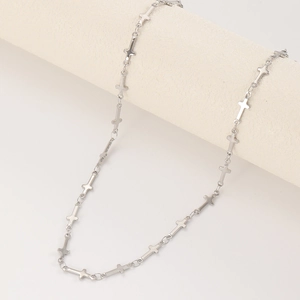 Collier à chaîne croisée en argent minimaliste sur un présentoir beige