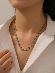 Detail of 304 stainless steel gold chain necklace with blue beads and green enamel leaves