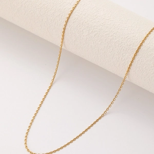Golden stainless steel O-chain necklace draped on a minimalist white textured pedestal