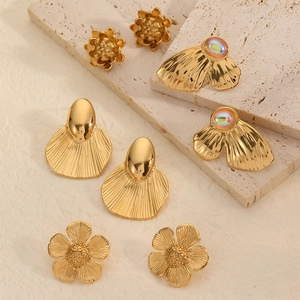 Close-up of assorted 18K gold plated floral and textured earrings on travertine
