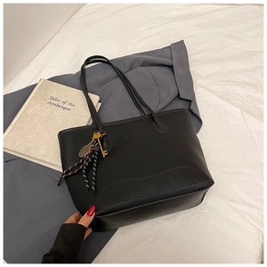 Detail of black pebbled leather tote bag featuring fashion charms and large capacity