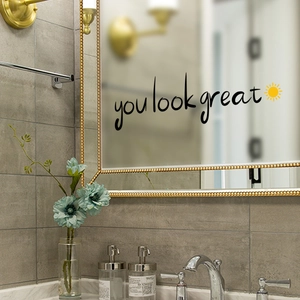 Detail of 'you look great' wall sticker with yellow sun icon on a modern bathroom mirror