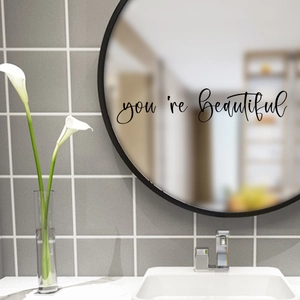 Close-up of You're Beautiful black script lettering decal on a round bathroom mirror