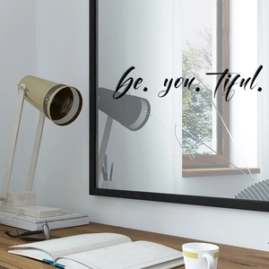 Macro detail of 'be.you.tiful.' black vinyl decal sticker on a minimalist mirror