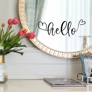 Close-up of black 'hello' vinyl decal with hearts on a gold framed round mirror