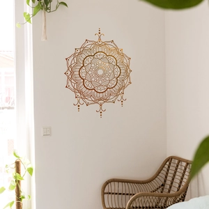 Detail of bohemian gold mandala wall decal on white wall with boho furniture and plant
