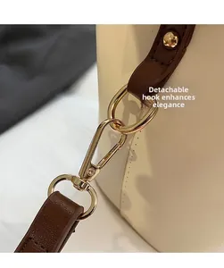 Detail of detachable golden hook and brown leather strap on cream bucket bag