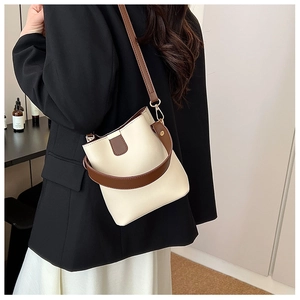 Model wearing a cream bucket bag with brown straps and gold metal hardware hooks
