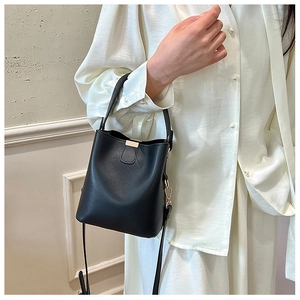 Detail of minimalist black leather bucket bag with gold hardware and removable strap
