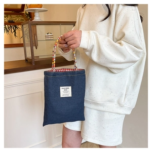 Detail of denim tote bag with colorful beaded handles and red checkered lining texture