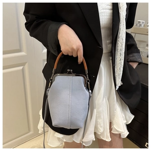 Detail of light blue denim kiss-lock crossbody bag with brown handles and silver clasp