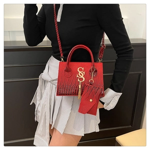 Detail of red crocodile texture crossbody bag with gold SS logo and tassel charm