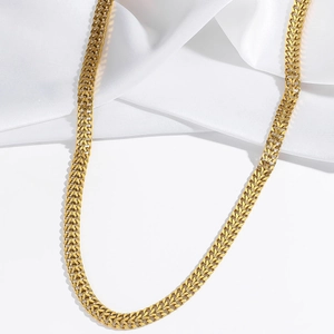 Vue macro détaillée d'un collier chaîne tressé doré sur un fond de tissu en soie blanche