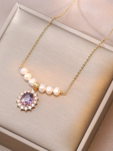 Close-up of gold necklace with oval purple stone surrounded by diamonds and pearls