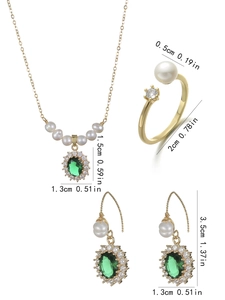 Detailed view of vintage jewelry set with emerald green stones and pearls on white background