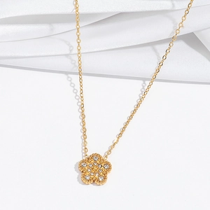 Détail d'un pendentif fleur dorée serti de zircons brillants sur une fine chaîne dorée