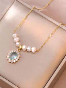 Detailed close-up of golden pearl necklace with a light blue gemstone pendant in a gift box