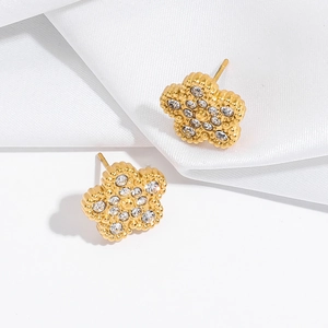 Détail de boucles d'oreilles fleur dorées avec zircons sur un tissu en soie blanche