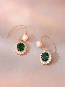 Detail of emerald green gemstone earrings with white pearls on elegant satin fabric