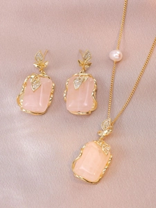 Close-up of pink gemstone jewelry set with gold leaf detail and pearl on satin fabric