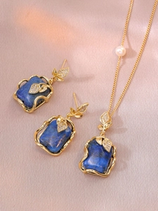 Detail of blue gemstone jewelry set with golden leaf motifs on pink satin background
