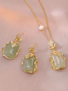 Close-up of gold-plated jewelry set with green gemstone pendants and pearl details