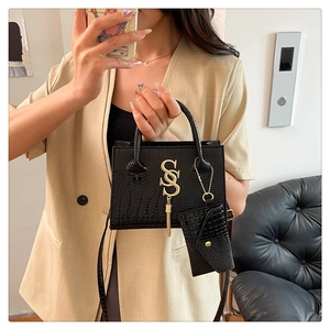 Detail of black crocodile texture handbag with golden metal S logo and mini bag attachment