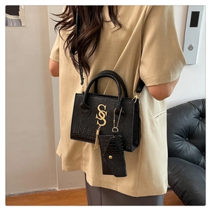 Close-up of black crocodile pattern crossbody bag with gold metal S logo and tassel detail