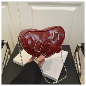 Détail d'un sac bandoulière coeur en cuir rouge foncé avec boucles argentées et chaîne