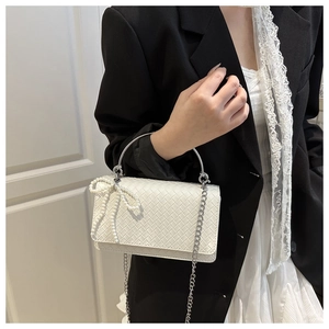 Close-up of white woven shoulder bag featuring a pearl bow and circular metal handle