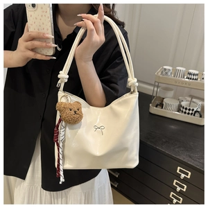 Close-up of off-white glossy shoulder bag with silver bow and cute bear keychain charm