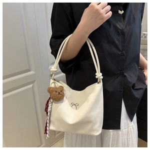 Detail of white glossy PU shoulder bag with silver bow accent and brown bear charm