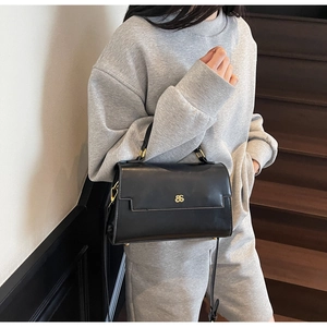 Detailed view of matte black leather handbag with gold metal logo on elegant stairs