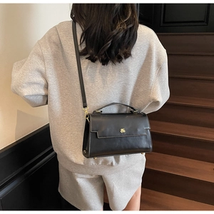 Detail shot of a black matte leather crossbody bag with a golden logo on a female model
