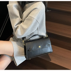 Detail of a black matte leather handbag with gold metal logo and adjustable shoulder strap