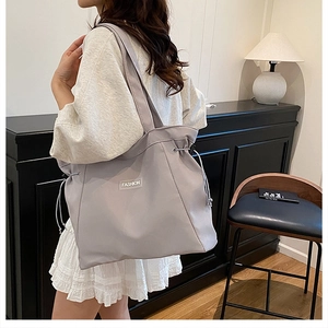 Detail of grey canvas tote bag with drawstring closure and fashion label on the front