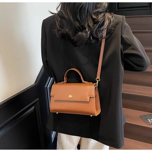 Detailed back view of a caramel leather crossbody bag worn by a model on a staircase