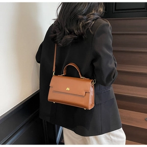 Detail view of a luxury brown leather handbag with gold logo and curved top handle