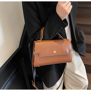Detail of caramel leather handbag with gold logo and adjustable shoulder strap on model