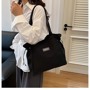 Detail of black tote bag featuring adjustable side drawstrings and fashion label tag