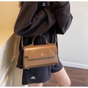 Detail of a brown leather crossbody phone bag with gold metal logo on a model