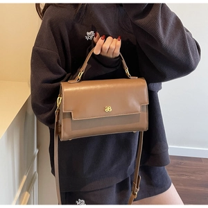Brown rectangular crossbody bag with gold metal logo and adjustable strap shown on model
