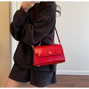 Detailed view of the red leather handbag featuring a signature gold metal logo buckle