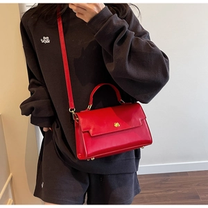 Side view of red glossy leather crossbody bag with gold clover lock on grey hoodie background
